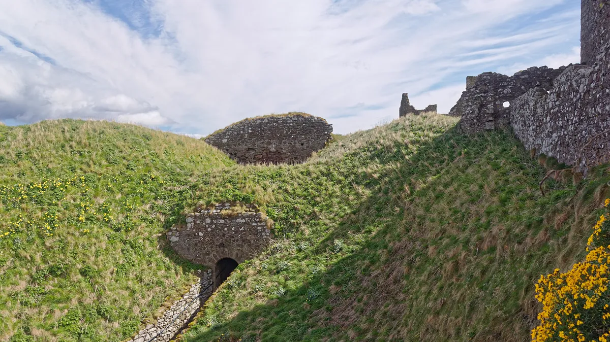Ruined Clifftop Fortress Walls and Grassy Earthworks Grassy earthworks and ruined stone walls of a clifftop fortress under a wide cloudy sky