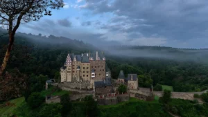 Stone castle with slate turrets above a misty forest valley in early light, a fitting scene for a throne of glass reading order guide