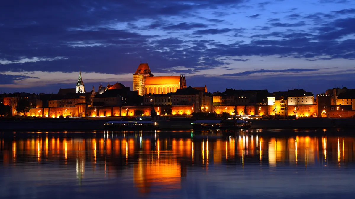 Old town skyline lit at night and reflected in a river, a city scene that suits an urban fantasy series setting